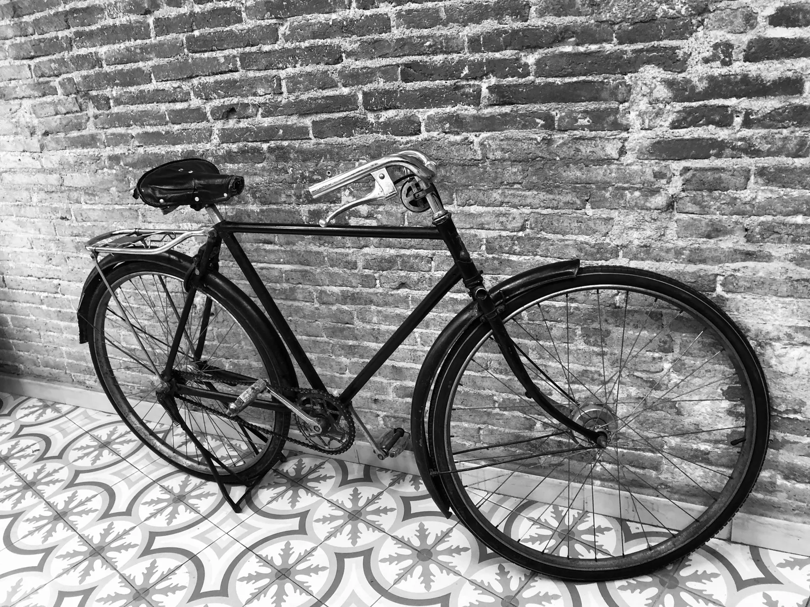 Schwarzes Fahrrad lehnt an einer Backsteinmauer, davor dekorativ gemusterte Bodenfliesen in Barcelona