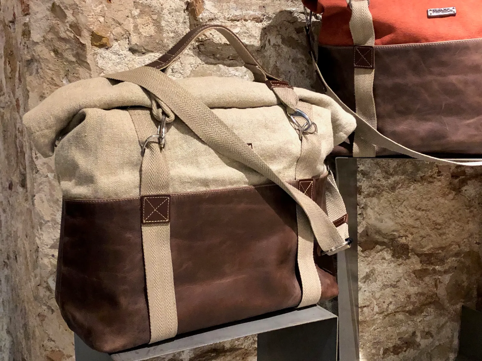 Handgefertigte Weekender-Taschen aus Leder und Leinen hängen an einer rustikalen Steinwand in einem Designladen
