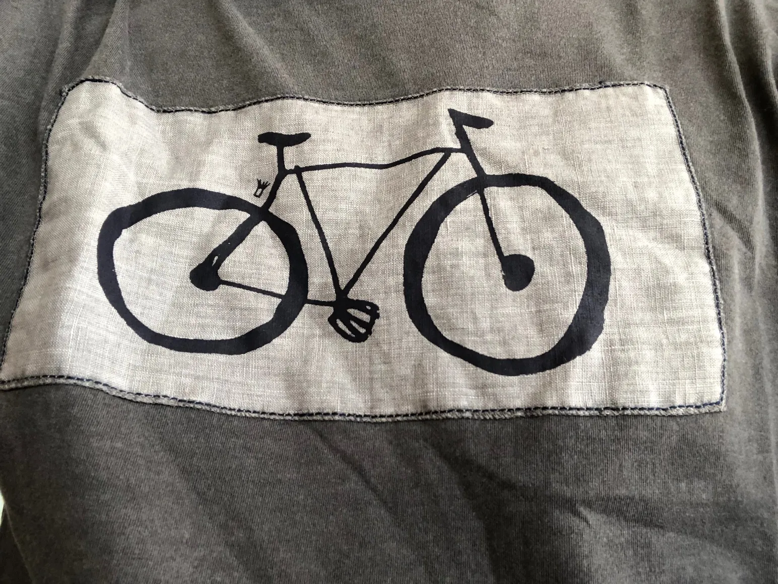 Grauer Pullover mit aufgenähtem Leinenstoff-Patch zeigt schwarze Fahrrad-Grafik