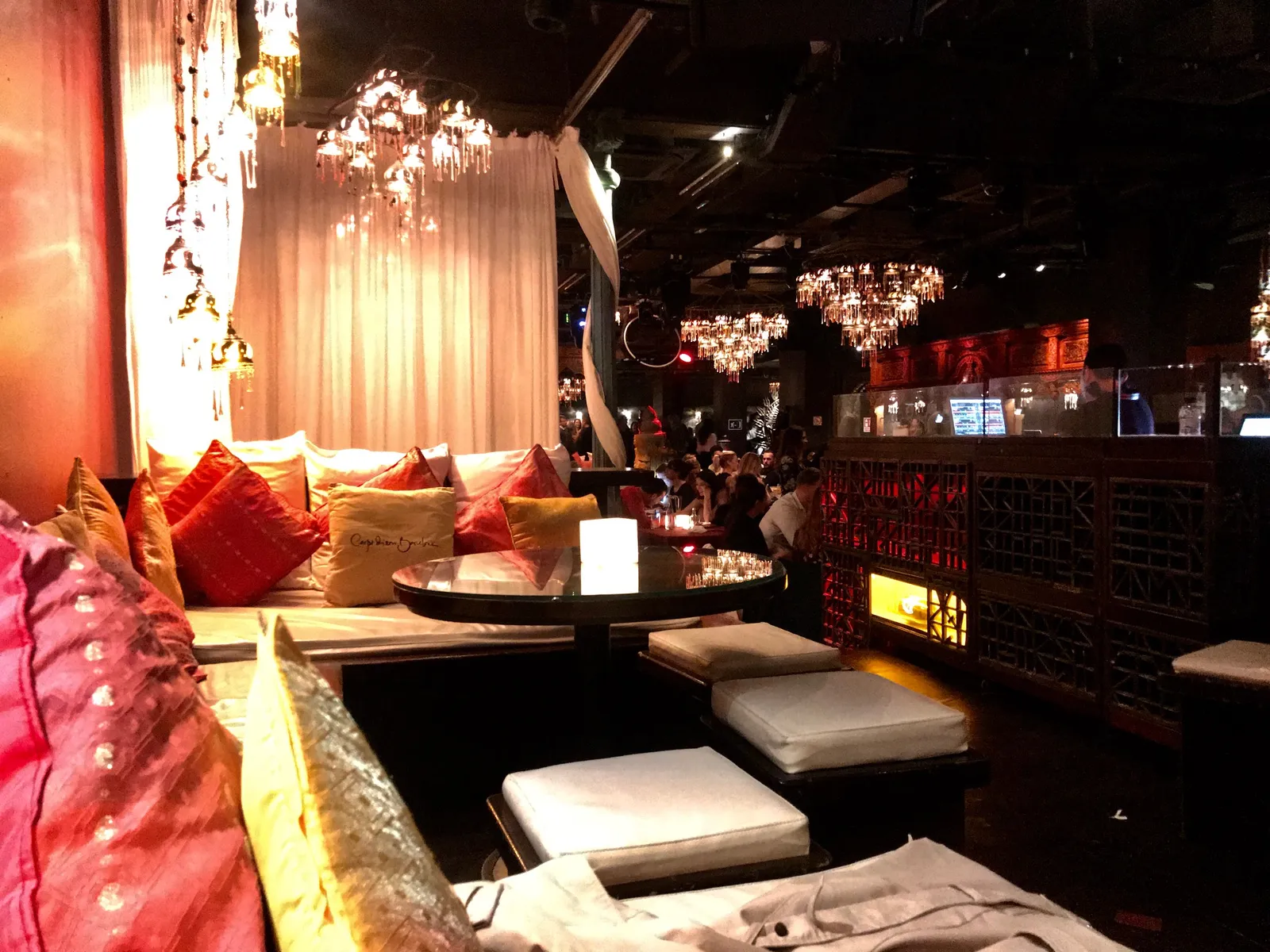 Luxuriöse Lounge-Ecke mit roten Samtkissen, Kristallleuchtern und gedimmtem Licht in elegantem Club mit orientalischem Flair