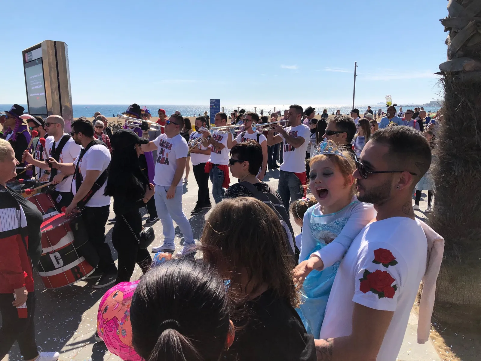 Große Menschenmenge in weißen Marathon-Shirts an der Strandpromenade, bunte Masken und ausgelassene Stimmung bei einer Parade