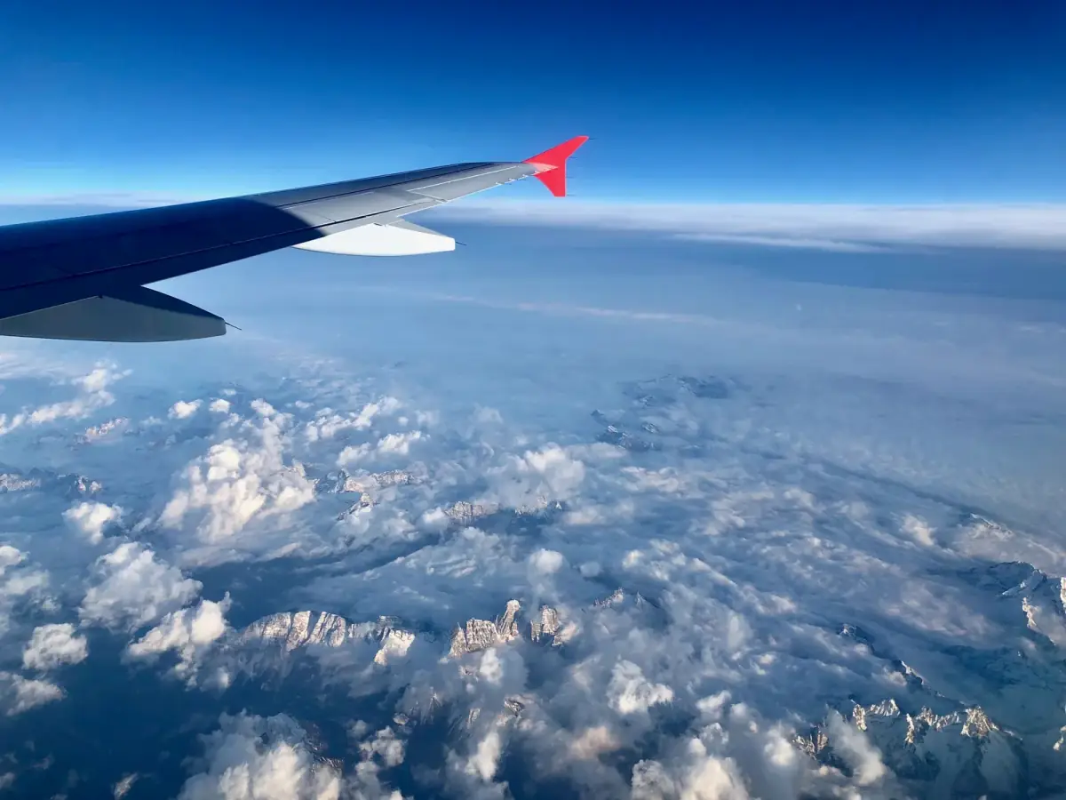 Flugzeugflügel mit rotem Winglet über schneebedeckten Alpen und Wolkenlandschaft während Rückflug nach Österreich