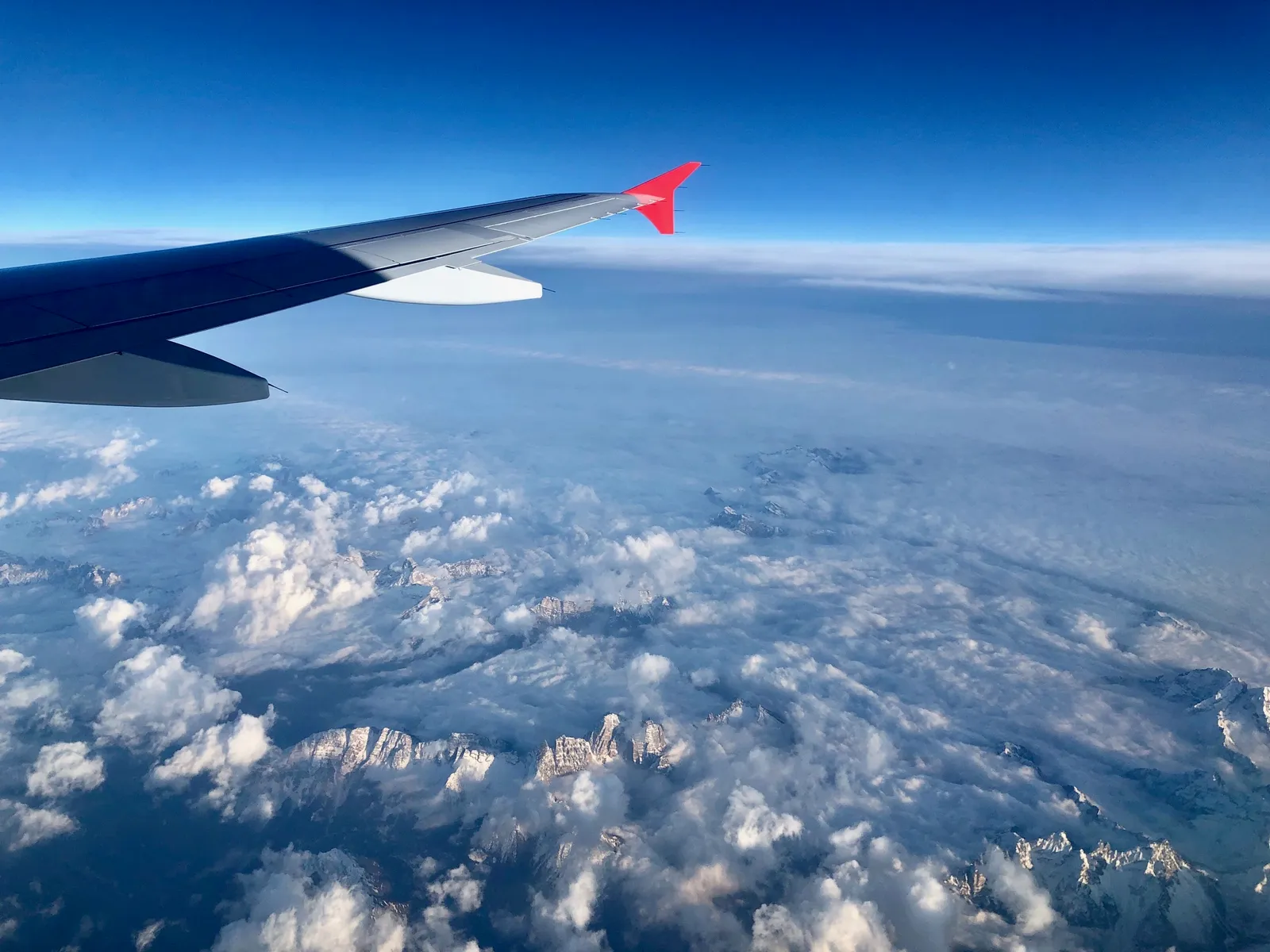 Flugzeugflügel mit rotem Winglet über schneebedeckten Alpen und Wolkenlandschaft während Rückflug nach Österreich