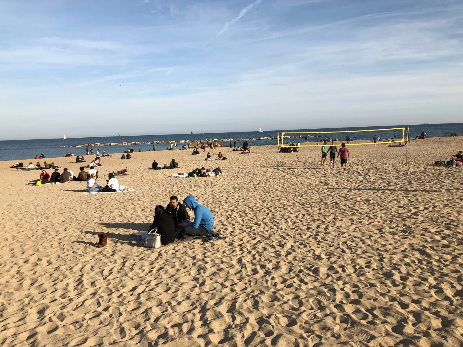 Freitagnachmittag am Strand von Barcelona: Menschen verschiedener Herkunft sitzen, spielen und entspannen im Sand