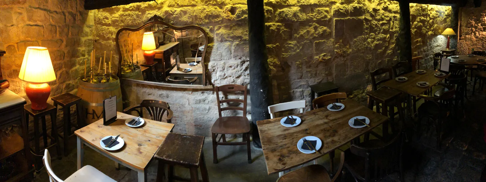 Rustikales Restaurant mit Steinwänden, Holztischen, gedeckten Plätzen und warmem Lampenlicht in traditionellem Ambiente