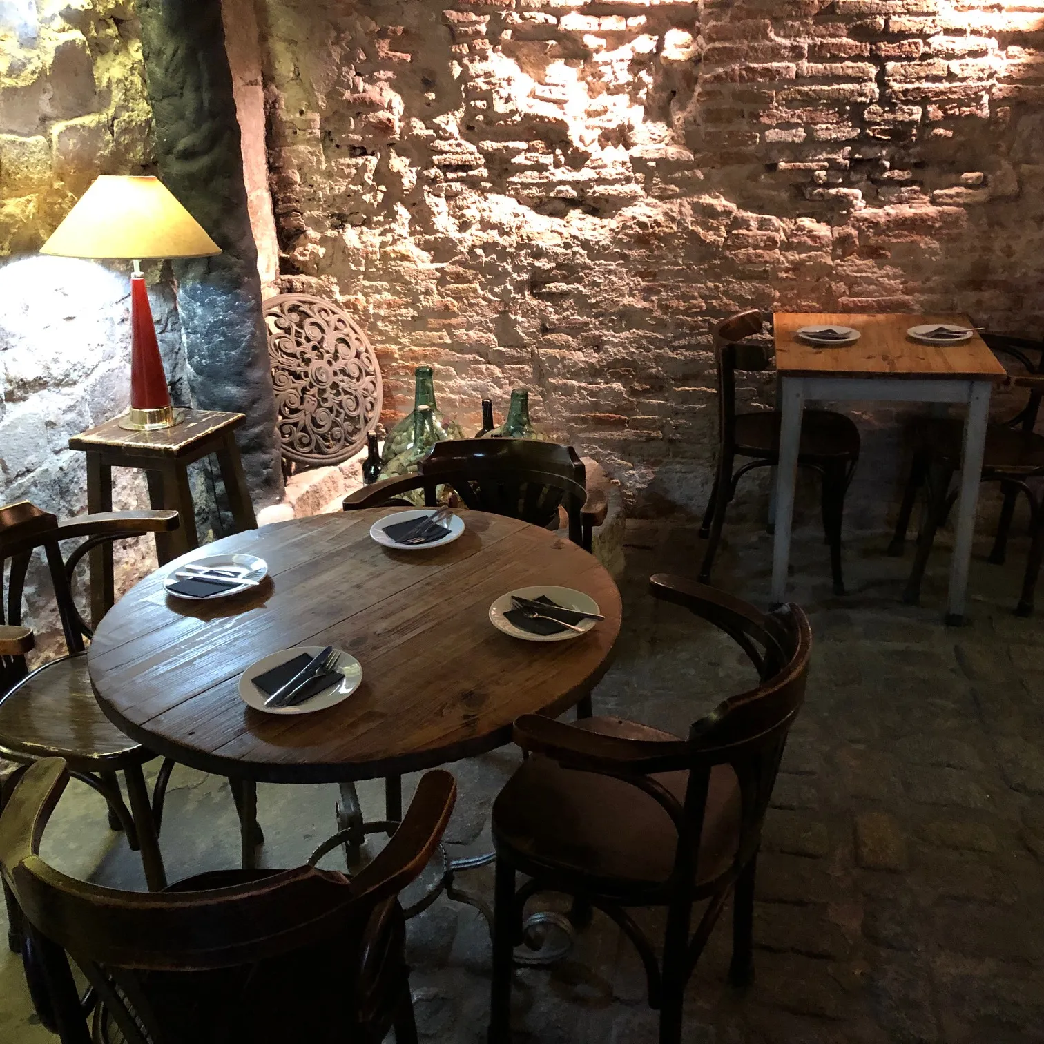 Rustikales Restaurant mit Steinwänden, gedeckten Tischen und Weinflaschen, warmes Lampenlicht schafft gemütliche Atmosphäre