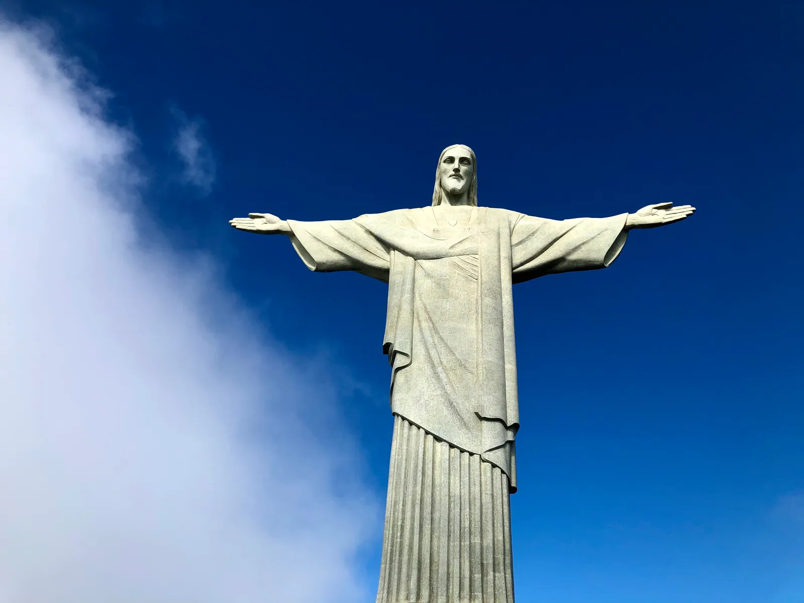 Monumentale Christusstatue mit ausgebreiteten Armen vor tiefblauem Himmel und einzelnen weißen Wolken