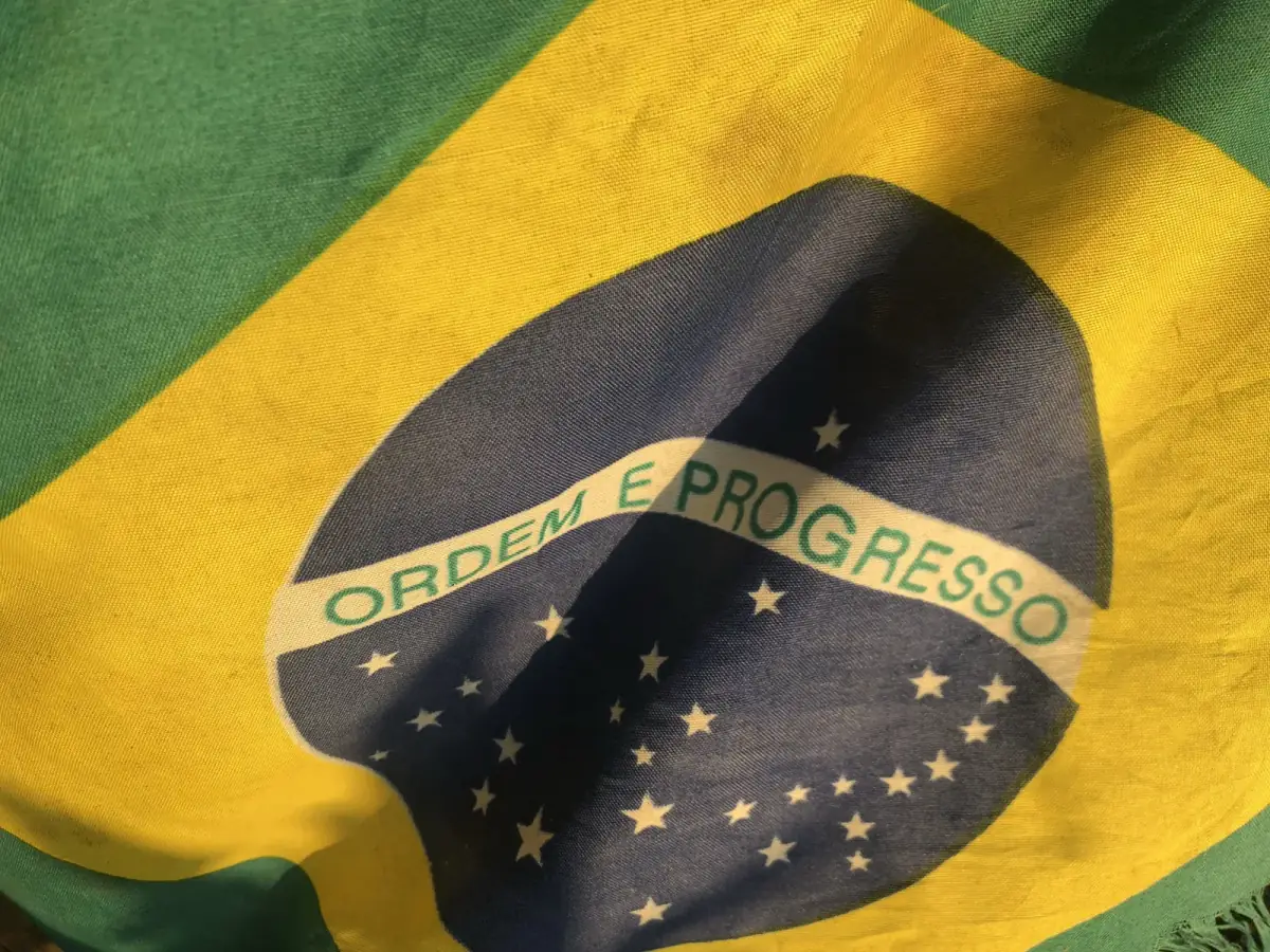 Brasilianische Flagge mit der Inschrift „Ordem e Progresso" weht im Abendwind vor grünem und gelbem Hintergrund
