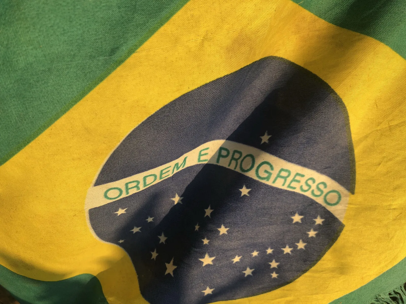 Brasilianische Flagge mit der Inschrift „Ordem e Progresso" weht im Abendwind vor grünem und gelbem Hintergrund