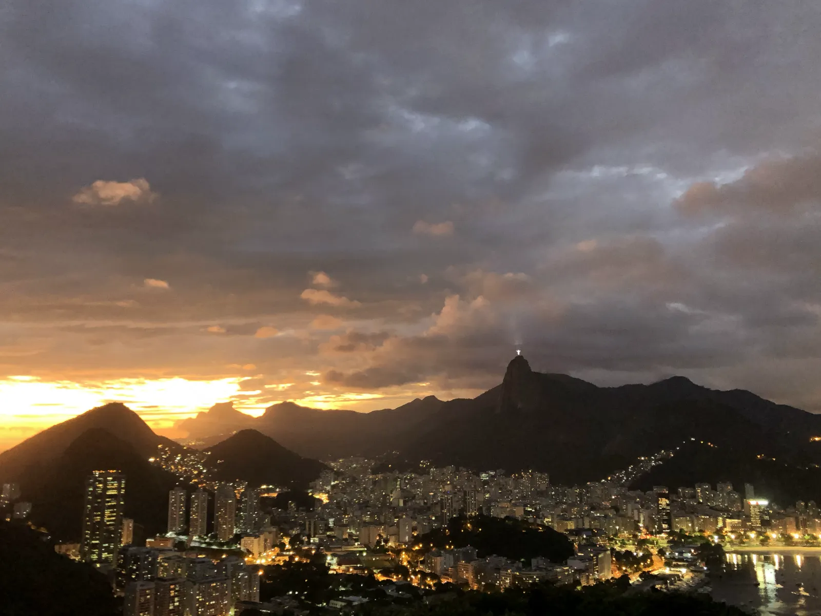 Sonnenuntergang über Rio de Janeiro mit leuchtender Stadt, Bergen und dramatischem Himmel