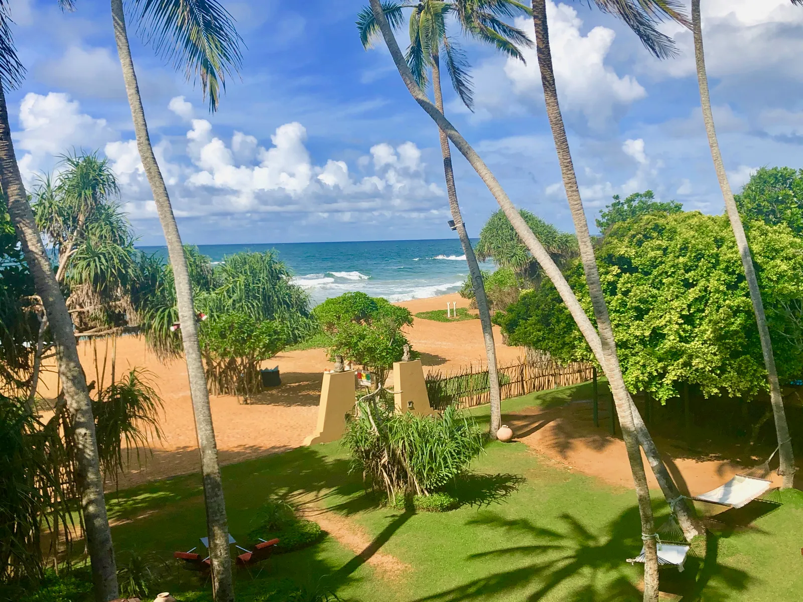 Tropischer Strandgarten mit Palmen, grünem Rasen und Blick auf Meer und Sandstrand unter blauem Himmel