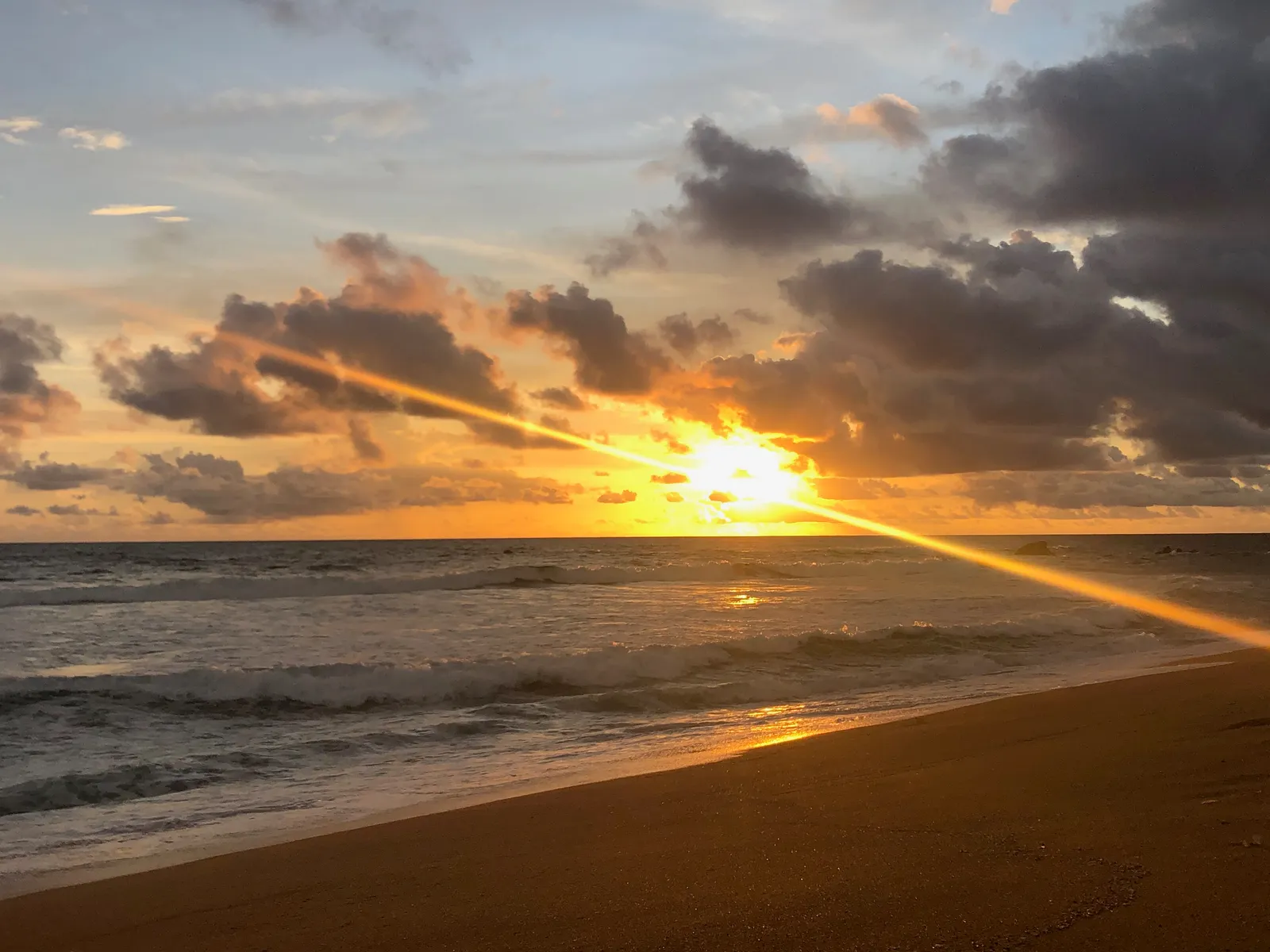 Sonnenuntergang über dem Meer mit dramatischen Wolken, goldenes Licht spiegelt sich auf dem Strand und Wasser