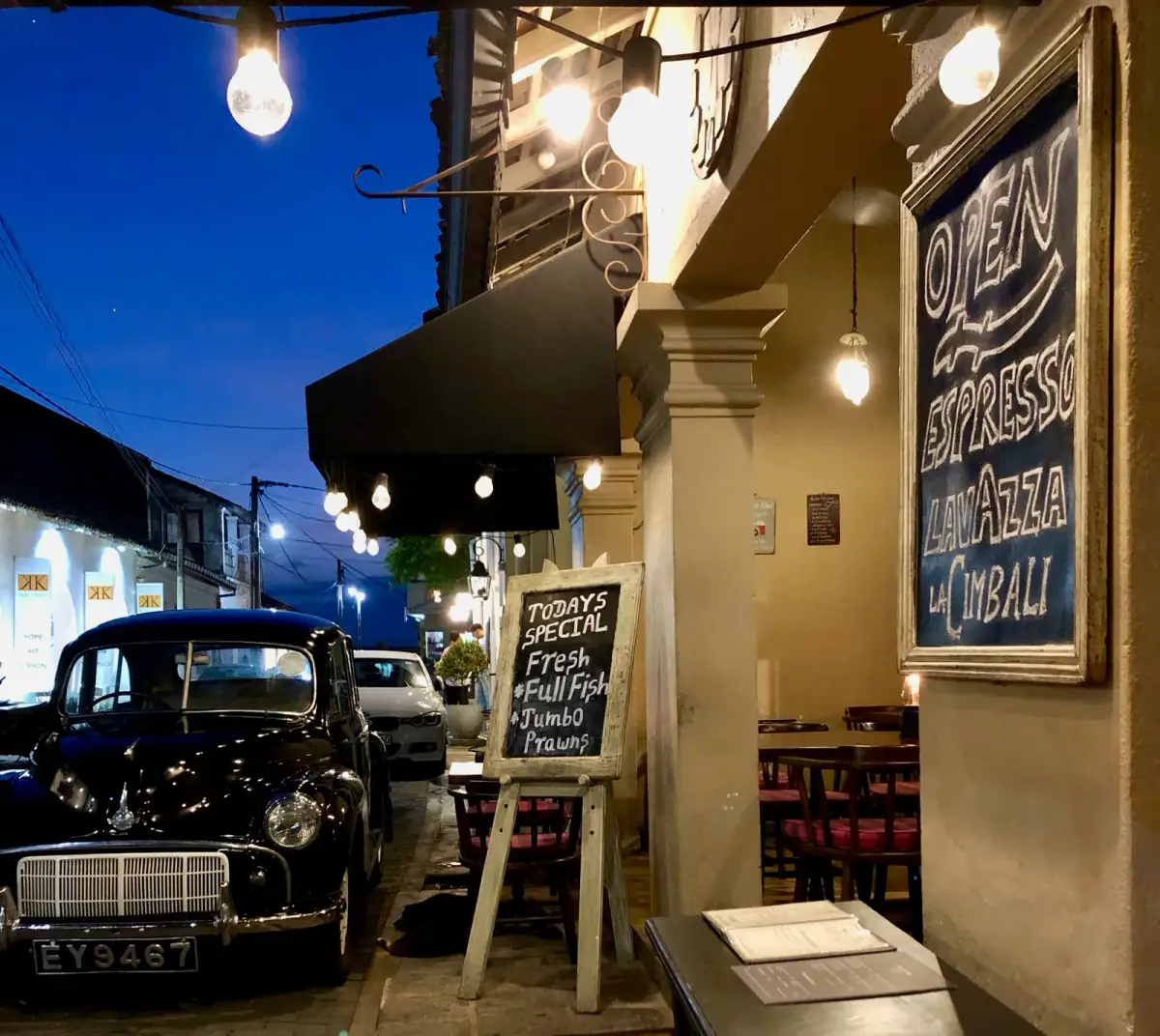 Nächtliche Straßenszene mit restauriertem Oldtimer, beleuchteter Restaurantfassade