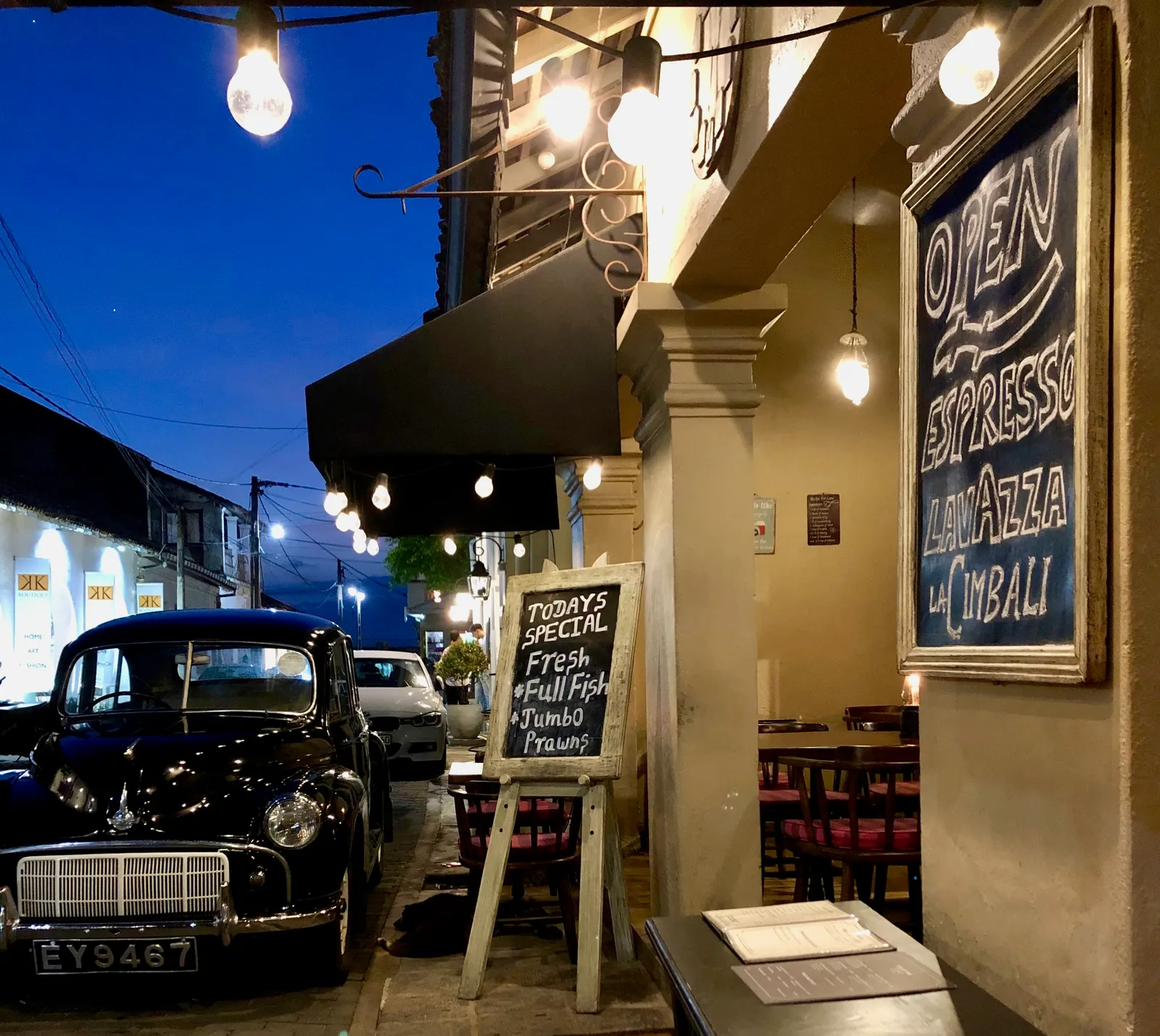 Nächtliche Straßenszene mit restauriertem Oldtimer, beleuchteter Restaurantfassade