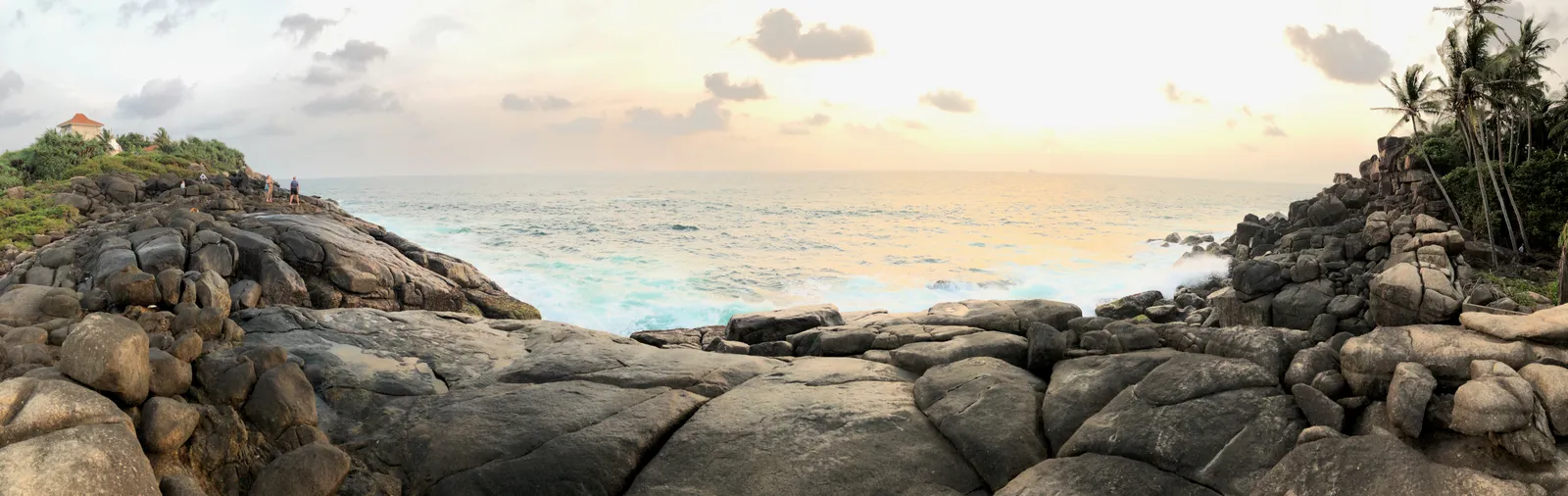 Felsenküste mit großen Granitblöcken, Palmen und türkisblauem Meer im Sonnenuntergang