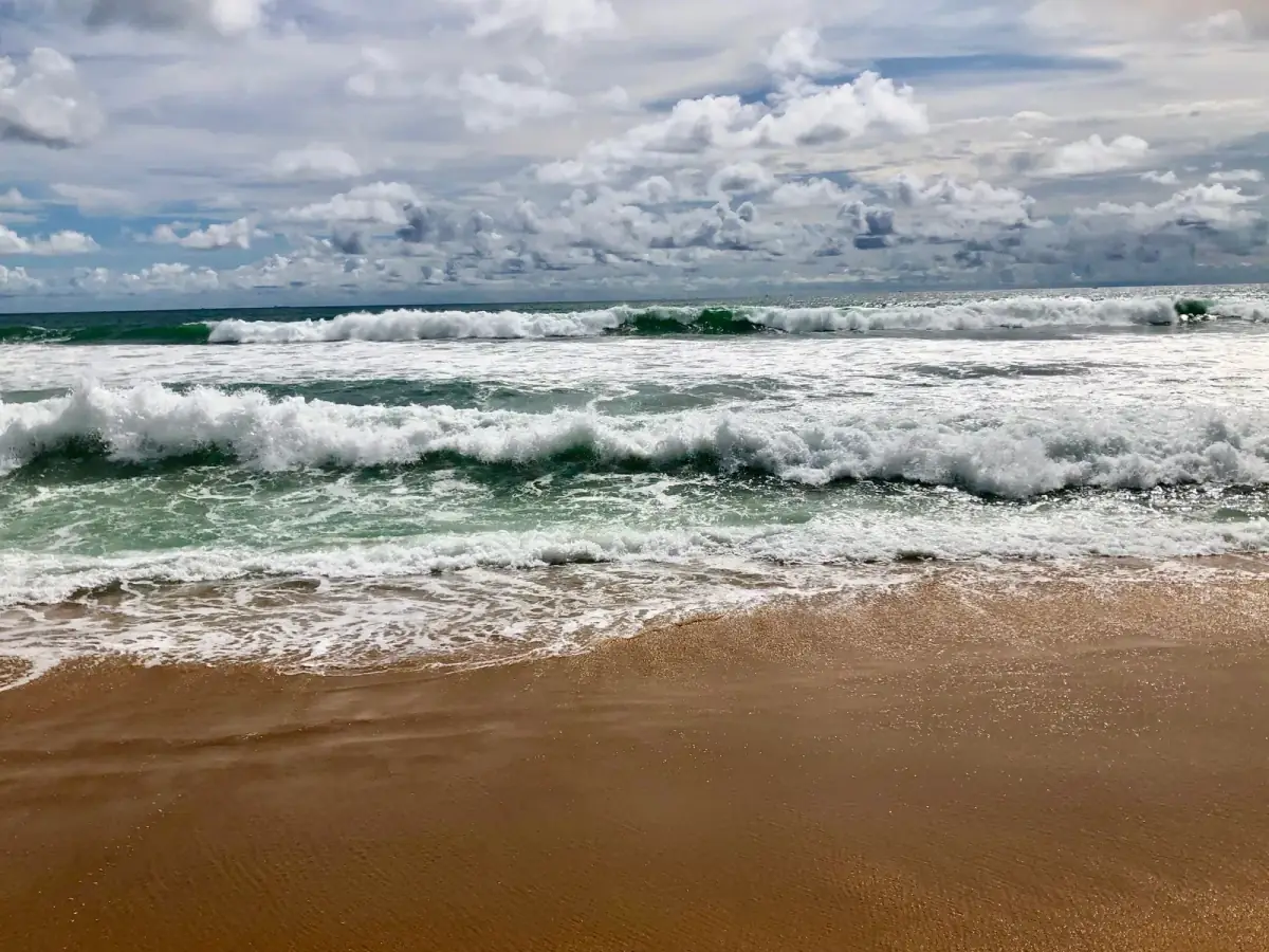 Brecher und Schaumkronen rollen auf türkisgrünem Wasser dem Sandstrand entgegen