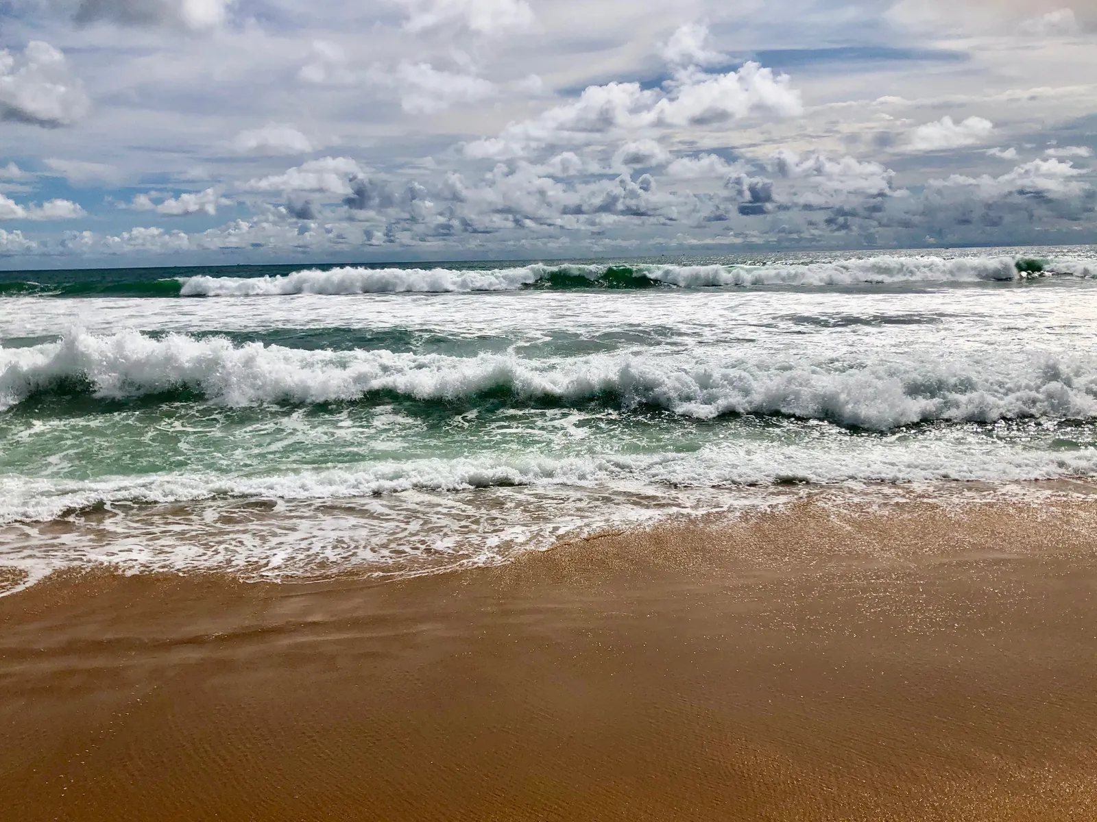 Brecher und Schaumkronen rollen auf türkisgrünem Wasser dem Sandstrand entgegen