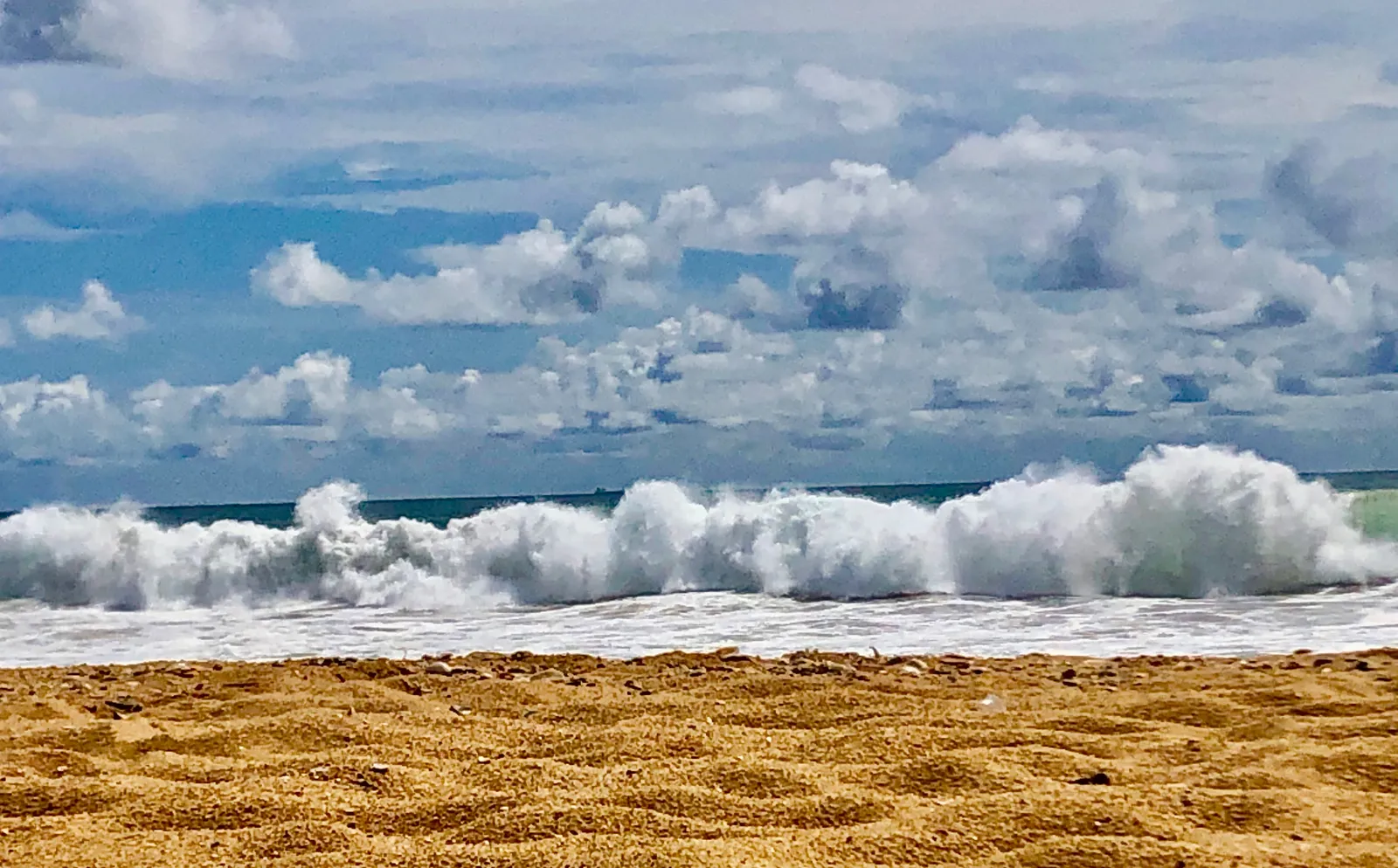 Breite Wellen mit weißer Gischt rollen auf einen breiten Sandstrand zu