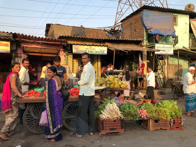 Belebter Straßenmarkt mit Gemüseständen, Verkäufern und Kunden in traditioneller Kleidung vor einfachen Läden