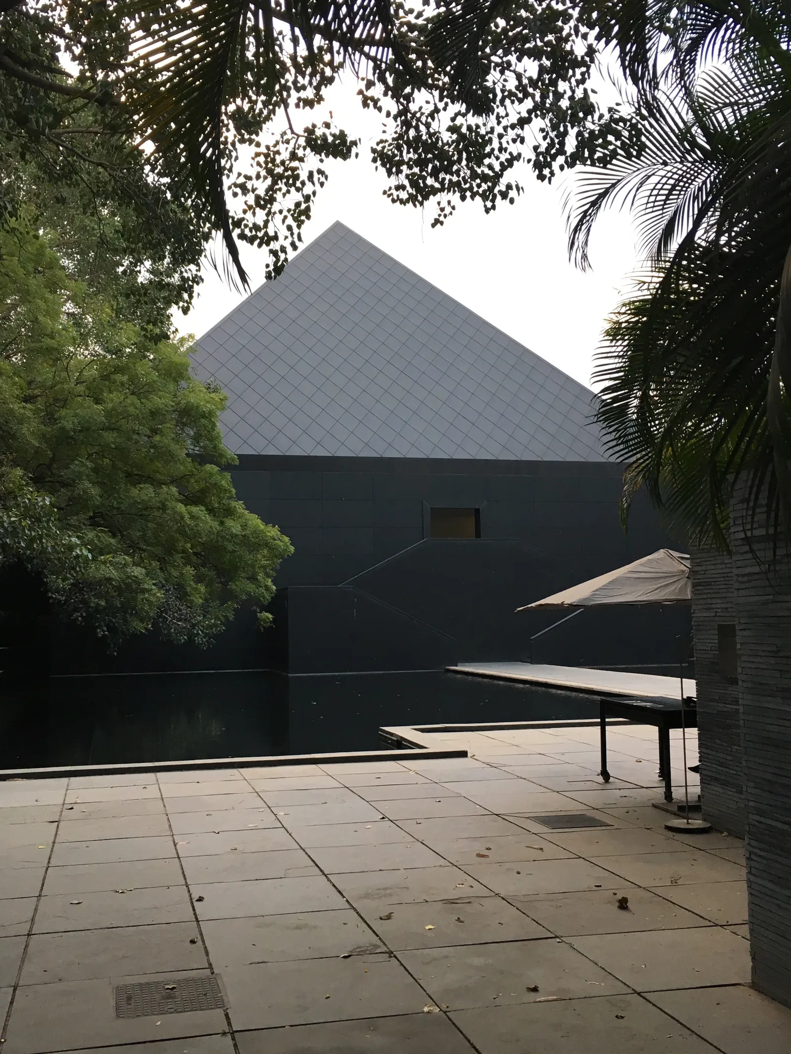 Modernes schwarzes Gebäude mit Pyramachendach in tropischer Umgebung, Terrasse mit Sonnenschirm und Meditationsatmosphäre