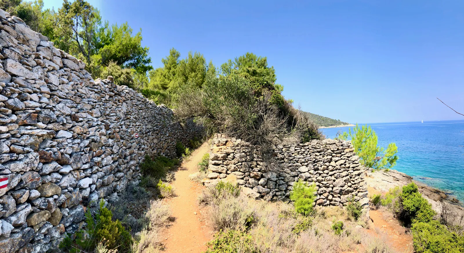 Küstenwanderweg mit historischen Steinmauern entlang mediterraner Vegetation und blauem Meer