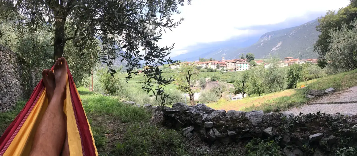 Hängematte zwischen Olivenbäumen mit Blick auf Dorf, See und grüne Hügellandschaft
