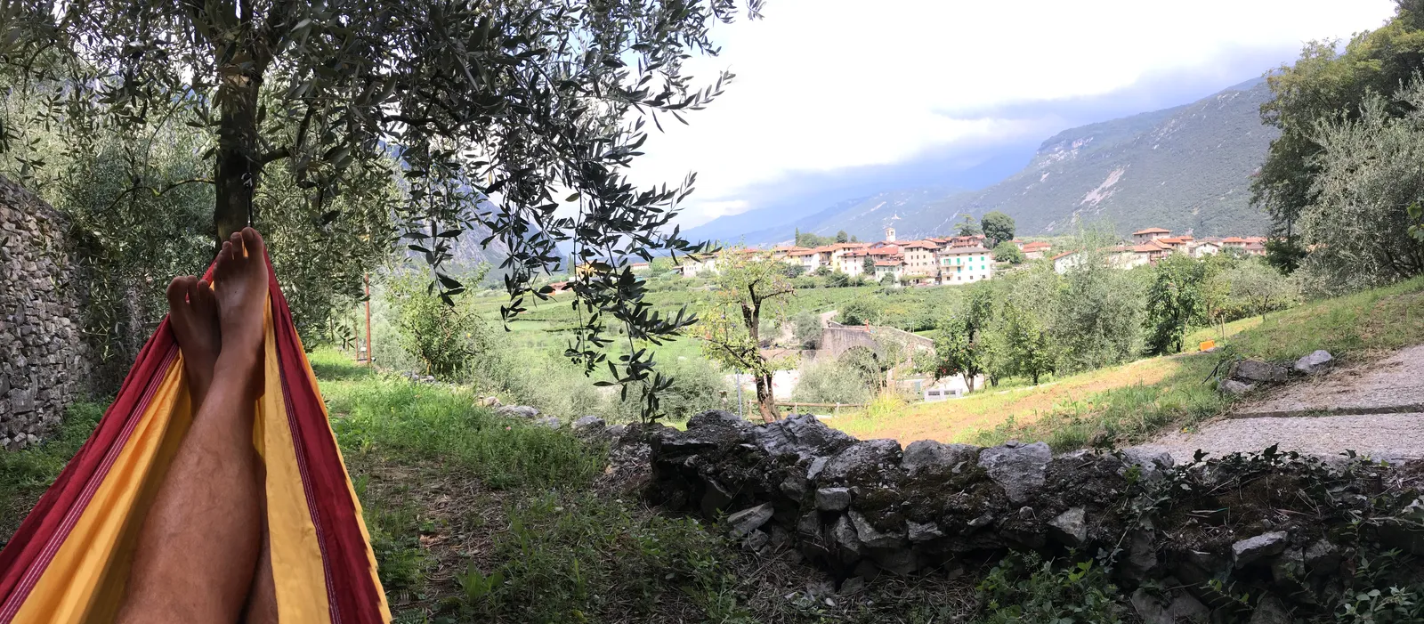 Hängematte zwischen Olivenbäumen mit Blick auf Dorf, See und grüne Hügellandschaft