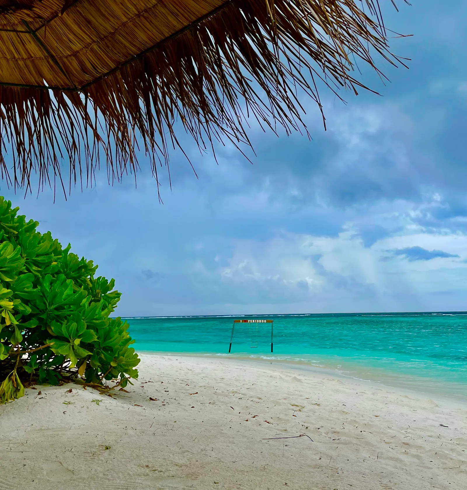 Tropischer Strand mit türkisblauem Meer, Palmdach und grüner Vegetation