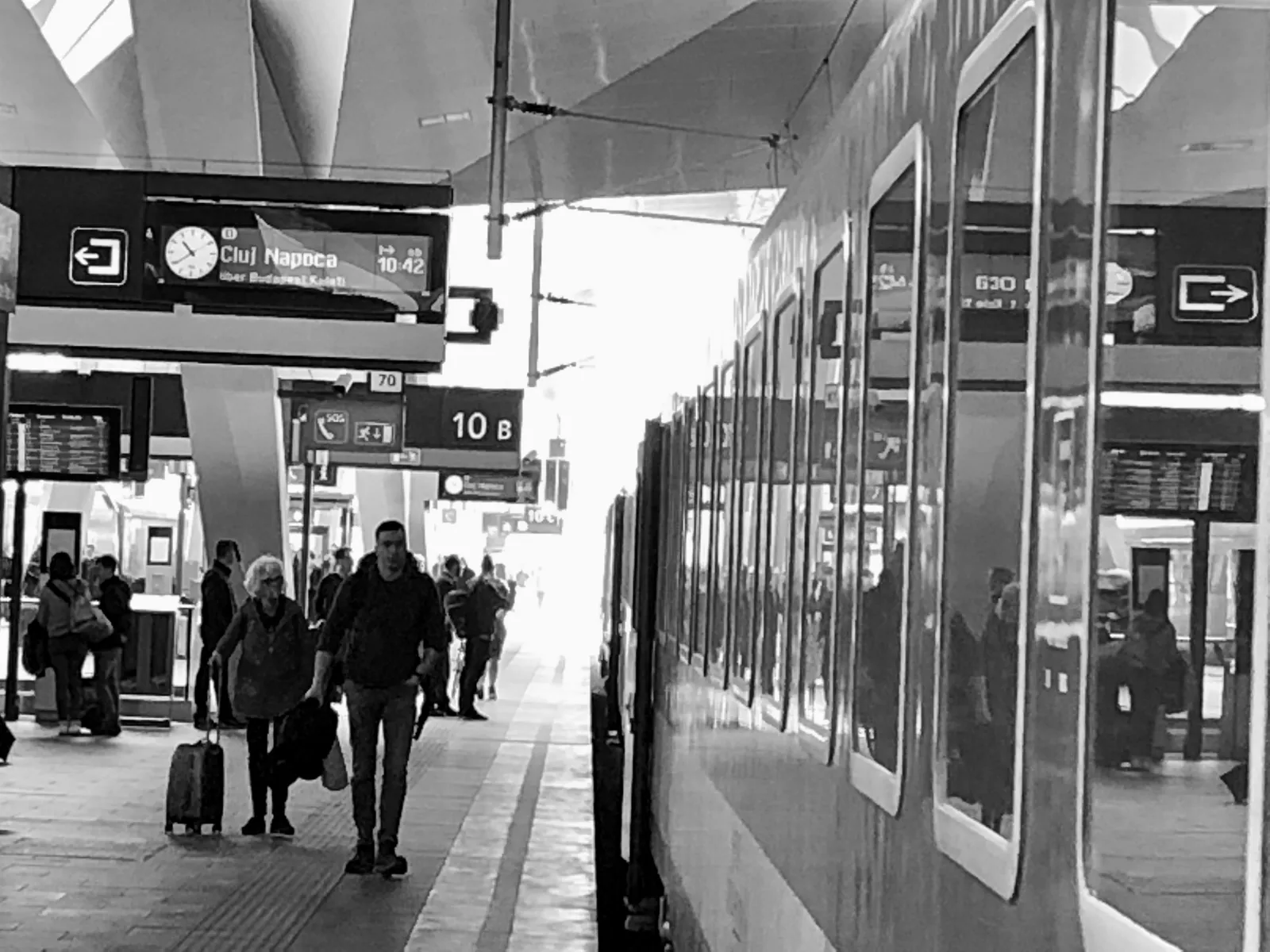 Bahnsteig mit Reisenden und modernem Zug, Anzeigetafeln zeigen Zielort Cluj-Napoca