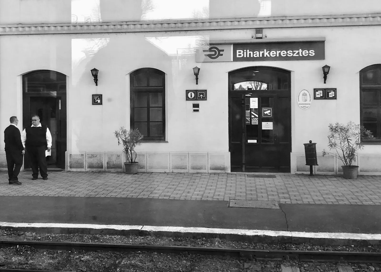 Zwei Männer stehen vor dem Bahnhof Biharkeresztes mit nostalgischem Retro-Flair, Schwarzweißaufnahme