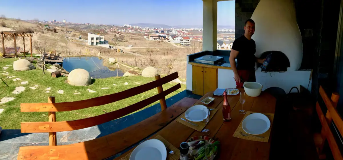 Esstisch unter freiem Dach mit Blick auf hügeliges Land, Menschen beim gemeinsamen Essen und Plaudern