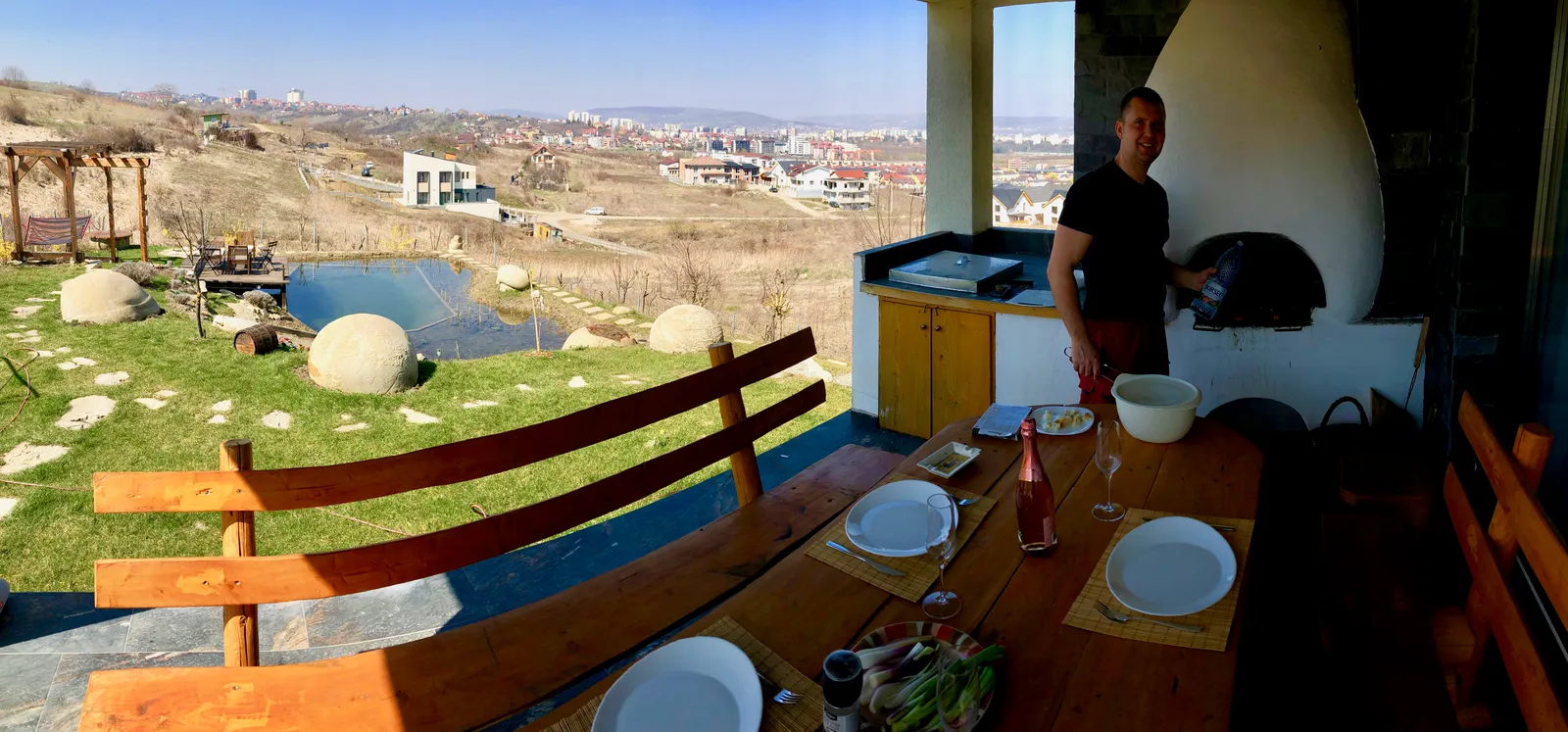 Esstisch unter freiem Dach mit Blick auf hügeliges Land, Menschen beim gemeinsamen Essen und Plaudern