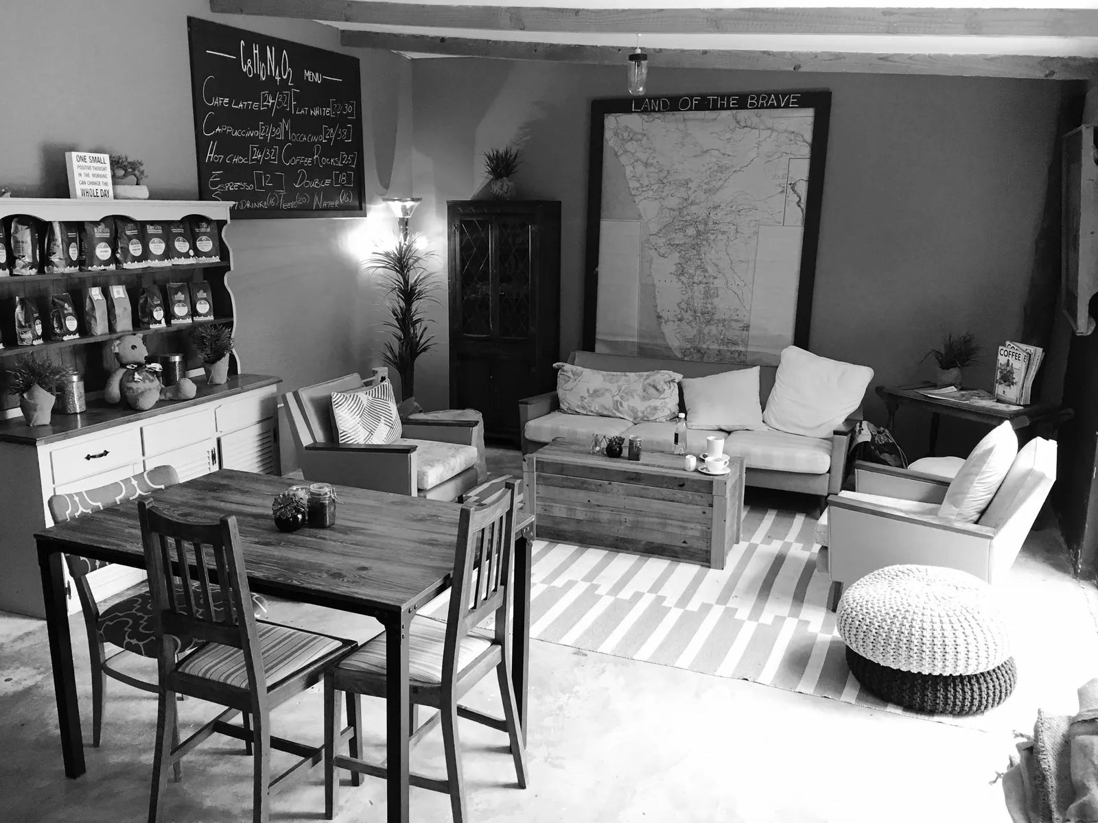 Gemütliches Café-Interieur mit Holztisch, Sesseln, Karte an der Wand und Kaffee-Regalen in Shabby-Chic-Stil