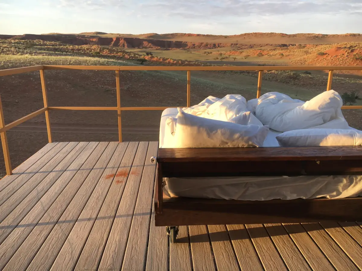 Gemütliches Bett mit weißer Bettwäsche auf einer Holzterrasse mit Metallgeländer