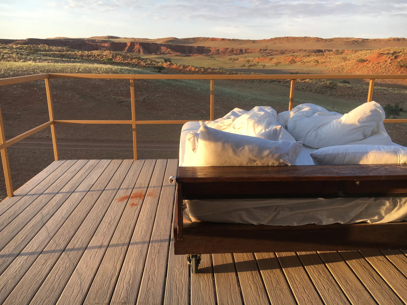 Gemütliches Bett mit weißer Bettwäsche auf einer Holzterrasse mit Metallgeländer