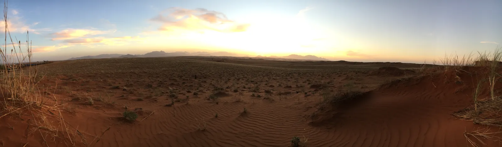 Weite Wüstenlandschaft bei Sonnenuntergang mit rötlichem Sand