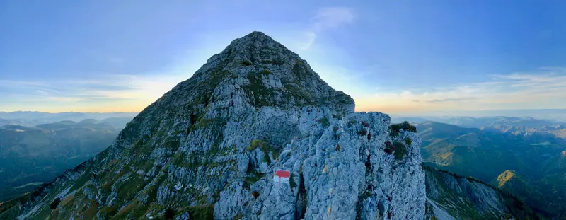 Wanderer auf einem schmalen Felsgrat eines spitzen Kalkbergs mit Blick über grüne Täler