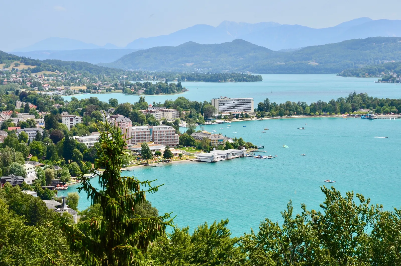 Türkisblauer Alpensee mit Uferstadt, Grünflächen und Bergen im Hintergrund an sonnigem Tag