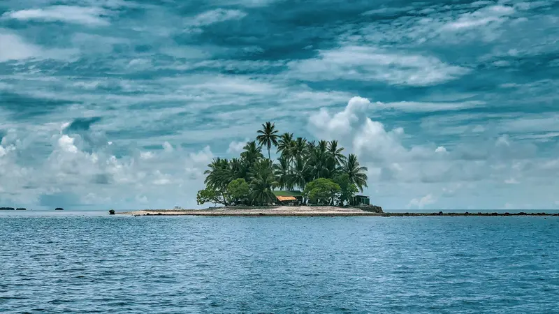 Kleine tropische Insel mit Palmen und Gebäude im türkisblauen Meer unter wolkigem Himmel