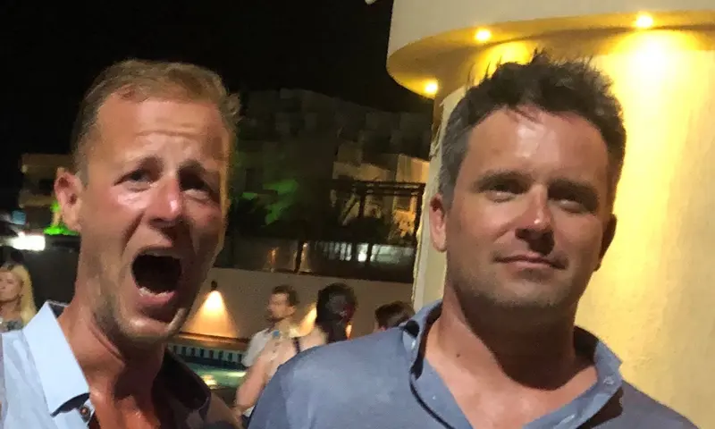 Zwei Männer schauen sich nachts auf einer Terrasse verdutzt an
