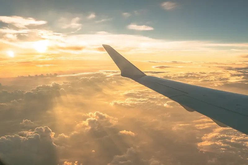 Flugzeugflügel vor goldener Abendsonne mit Wolkendecke und blauem Himmel während eines Flugs