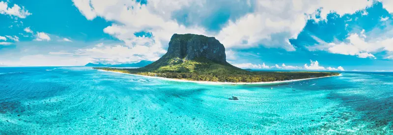 Türkisblaues Meer umgibt eine grüne Insel mit steilem Felsgipfel unter blauem Himmel mit weißen Wolken