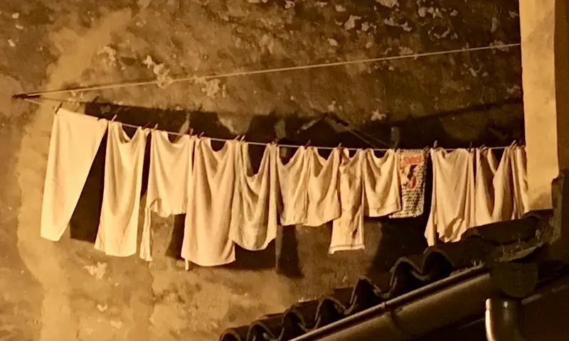 Wäsche hängt auf einer Leine vor einer verwitterten Hauswand in dämmrigem Licht