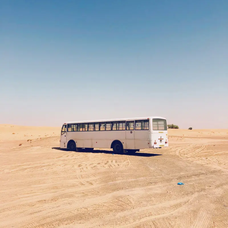 Weißer Bus steht einsam in der flachen Wüstenlandschaft unter klarem Himmel, Sandspuren sichtbar