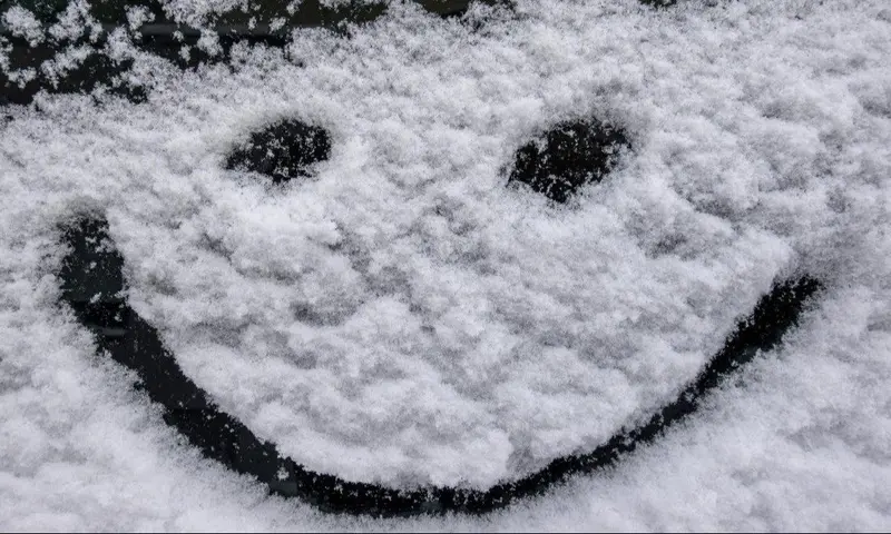 Smiley-Gesicht aus schwarzen Objekten auf weißer Schneedecke gezogen