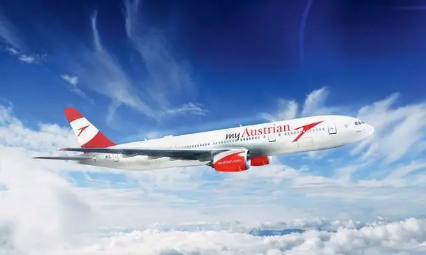 Austrian-Airlines-Flugzeug mit rot-weißer Lackierung fliegt über Wolkendecke am blauen Himmel