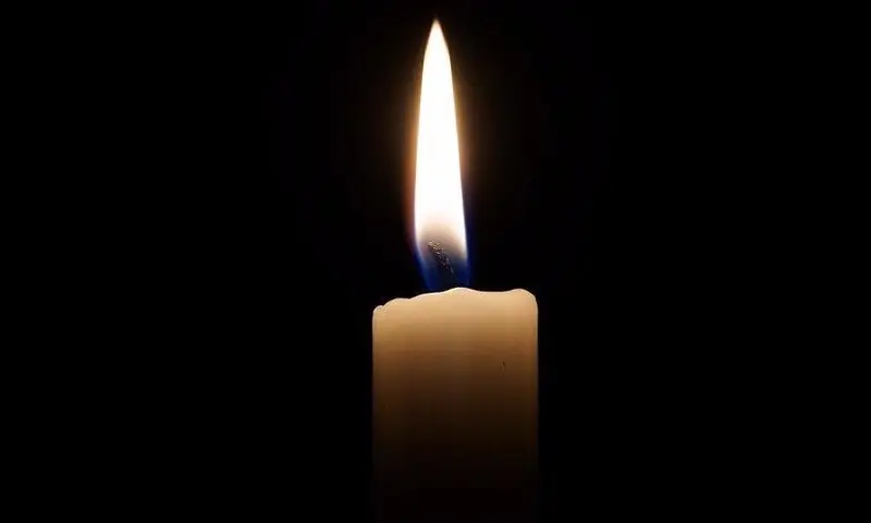 Eine brennende Kerze mit weißer Flamme vor schwarzem Hintergrund symbolisiert Abschied und Erinnerung