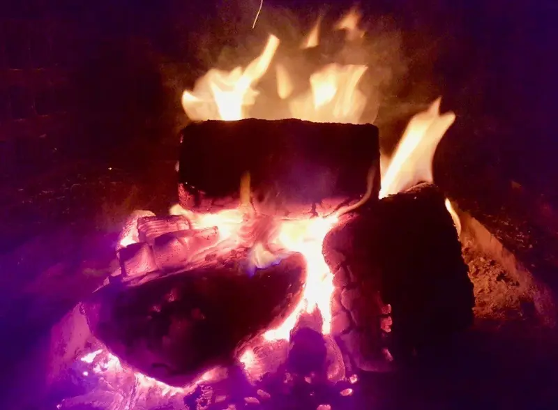 Brennendes Lagerfeuer in der Nacht mit intensiven Flammen in Orange-, Rot- und Violetttönen, Holzscheite glühen in der Hitze