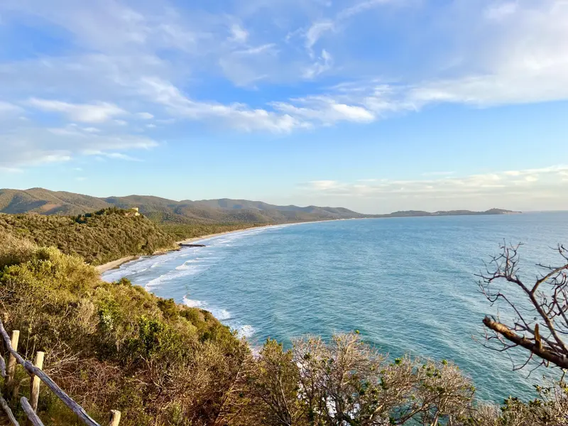 Küstenlandschaft der Maremma mit grünen Hügeln, Sandstrand und türkisblauem Meer unter wolkenlosem Himmel