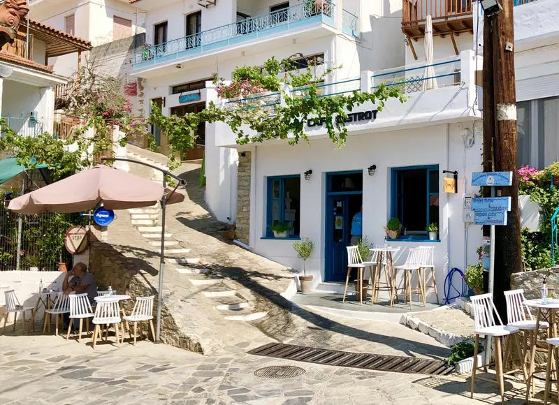 Idyllischer Platz mit weißen Häusern, blauen Türen, Sonnenschirm und Stühlen in mediterraner Atmosphäre
